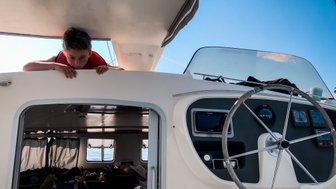 Ein Junge mit einer Rettungsweste lehnt über die Reling eines Segelboots und schaut neugierig nach draußen.