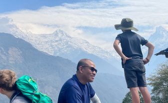 Ein Junge mit einem Hut steht nachdenklich auf einem Felsen und blickt auf die majestätischen schneebedeckten Berge.