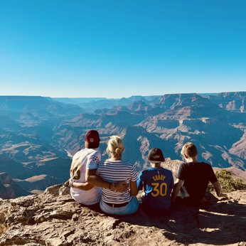 Eine Gruppe von vier Personen sitzt am Rand des Grand Canyon und genießt die atemberaubende Aussicht auf die Landschaft.