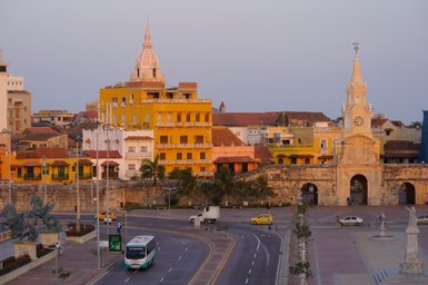 Bunte Gebäude mit historischen Fassaden und einer markanten Kirchturmspitze prägen die Skyline von Cartagena bei Sonnenuntergang.