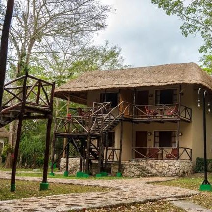 Ein zweigeschossiges Hotelgebäude mit Strohdach, umgeben von üppigem Grün und einem gepflasterten Weg.