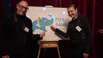 Ein Mann und eine Frau stehen lächelnd vor einem bunten Elefantenbild, das auf einer Staffelei präsentiert wird.