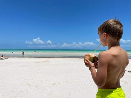 Kind trinkt frisches Kokosnusswasser am Strand von Puerto Morelos – Mexiko Familienreise