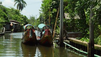 Traditionelle Longtailboote ruhen am Ufer eines Kanals – Thailand mit Kindern