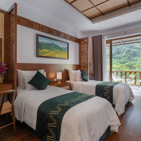 Zwei Einzelbetten mit eleganter Bettwäsche stehen in einem stilvollen Zimmer mit Blick auf die grüne Landschaft.