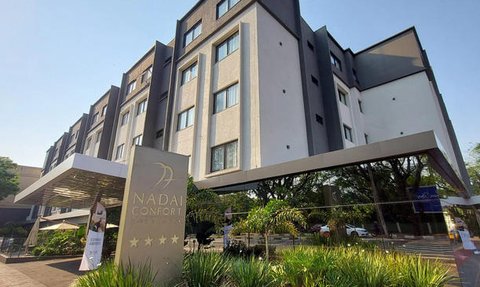 Das moderne Hotel Nadia Confort beeindruckt mit seiner stilvollen Architektur und einladender Pflanzenlandschaft im Vordergrund.