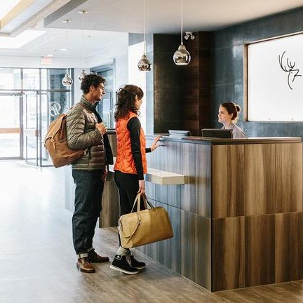 Ein Paar steht an der Rezeption eines modernen Hotels, während die Empfangsdame freundlich mit ihnen spricht.