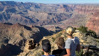 Drei Kinder stehen am Rand des Grand Canyon und bewundern die beeindruckende Aussicht auf die tiefen Schluchten und Felsen.
