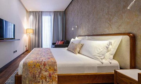 Ein stilvolles Hotelzimmer mit einem großen Bett, buntem Überwurf und einem gemütlichen Sessel in der Ecke.