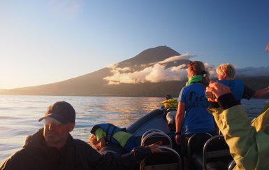 Eine Gruppe von Menschen auf einem Boot genießt den Sonnenuntergang mit einem majestätischen Berg im Hintergrund.