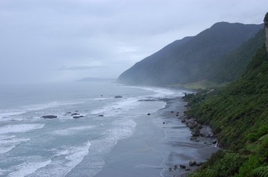 Eine ruhige Küstenlandschaft mit sanften Wellen, die an einen steinigen Strand schlagen, umgeben von grünen Hügeln.