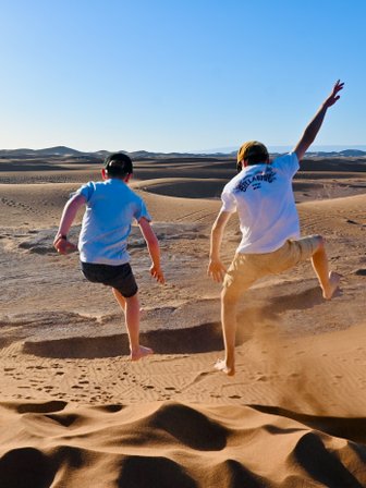 Kinder springen und haben Spaß auf den weiten Sanddünen der Sahara – Marokko Familienreise