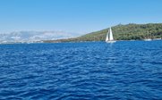 Ein Segelboot gleitet über das tiefblaue Wasser, während im Hintergrund grüne Hügel und Berge sichtbar sind.