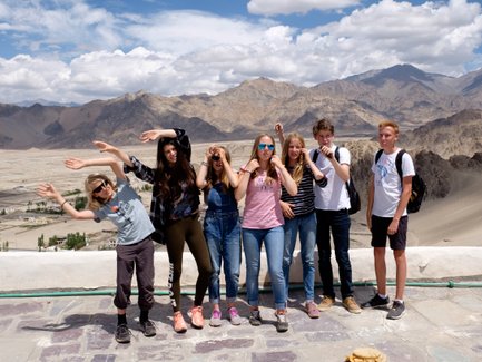 Eine Gruppe von Teenagern posiert fröhlich vor einer beeindruckenden Berglandschaft mit Wolken am Himmel.