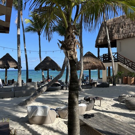Ein sonniger Strand mit Palmen, Liegen und Strohhütten, die eine entspannte Urlaubsatmosphäre schaffen.