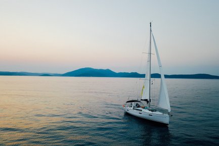 Ein Segelboot gleitet sanft über das ruhige Wasser, umgeben von sanften Hügeln im Hintergrund und einem zarten Abendhimmel.