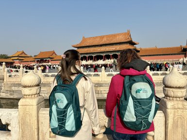 Zwei Frauen mit Rucksäcken stehen am Wasser und betrachten die beeindruckende Architektur der Verbotenen Stadt in Peking.