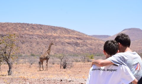 Zwei Kinder beobachten aus der Ferne eine Giraffe - Namibia Rundreise mit Kindern