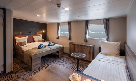 Ein modernes Kabineninnere mit zwei Betten, einem Tisch und Fenstern, die einen Blick auf das Meer bieten.