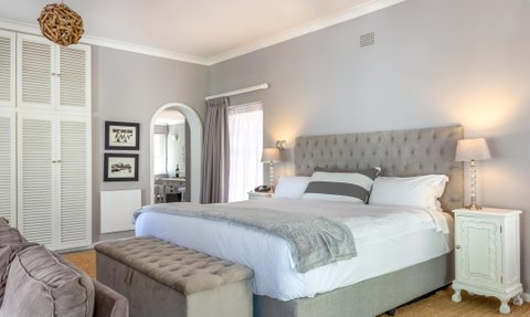 Ein elegantes Schlafzimmer mit einem großen, gepolsterten Bett und einem gemütlichen Sitzbereich, umgeben von sanften Farben.