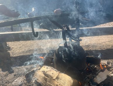Ein rauchender Lagerfeuerplatz mit einem Kessel, der über dem Feuer hängt, während Würstchen grillen.
