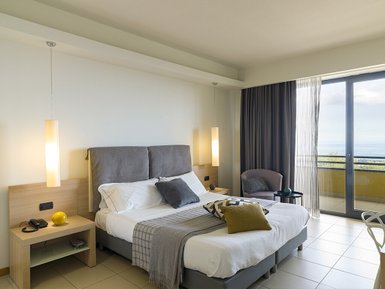 Ein modernes Hotelzimmer mit einem großen Bett, eleganten Lampen und einem Balkon mit Meerblick.