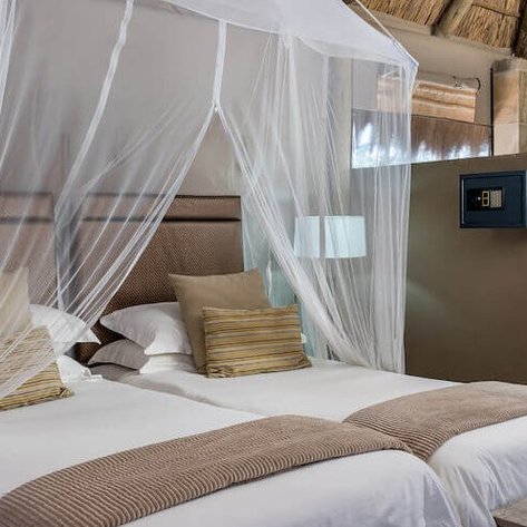 Ein elegantes Zimmer mit zwei Einzelbetten, umgeben von einem schützenden Moskitonetz und modernen Annehmlichkeiten.