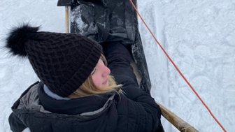 Ein Mädchen sitzt auf einem Schlitten, während sie in einer verschneiten Landschaft nach vorne schaut, umgeben von Schnee.