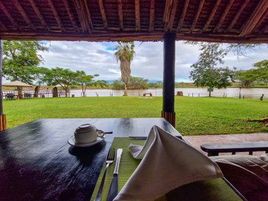 Ein Blick auf eine grüne Wiese mit einem Fluss im Hintergrund, während ein Tisch mit Geschirr im Vordergrund steht.
