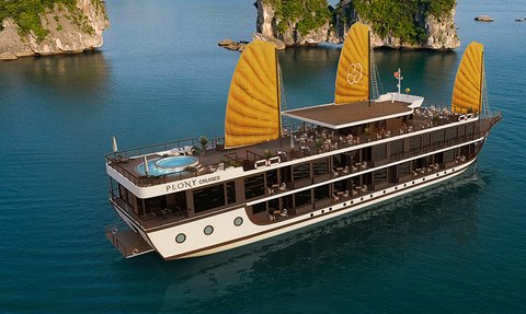 Ein elegantes Kreuzfahrtschiff mit gelben Segeln gleitet über das ruhige Wasser der Lan Ha Bucht, umgeben von grünen Felsen.