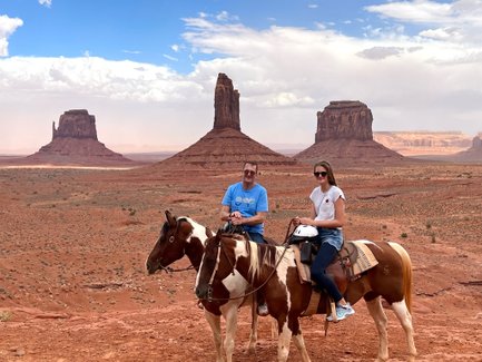 Ein Mann und eine Frau reiten auf Pferden vor der beeindruckenden Kulisse der Monument Valley Felsen.