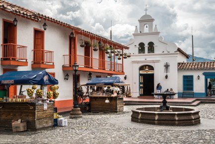 In einer malerischen Stadtansicht sind bunte Stände mit frischen Früchten und Souvenirs um einen zentralen Brunnen gruppiert.