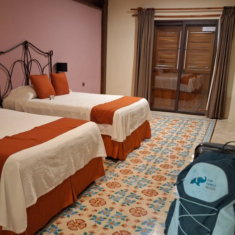 Ein gemütliches Hotelzimmer mit zwei Einzelbetten, bunten Fliesen und einem großen Fenster, das Tageslicht hereinlässt.