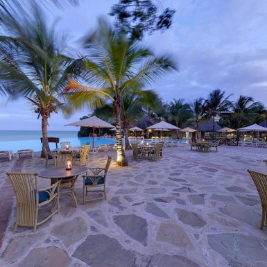 Ein einladender Strandresort-Bereich mit Palmen, Tischen und Stühlen, ideal für entspannte Abende am Meer.