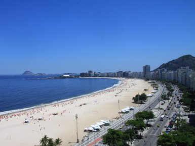 Ein weitläufiger Blick über den sonnigen Strand von Copacabana, gesäumt von Palmen und Menschen, die entspannen und Spaß haben.