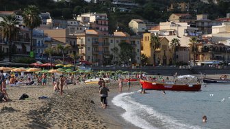 Ein belebter Strand in Giardini Naxos mit vielen Menschen, die sich entspannen und im Wasser spielen.