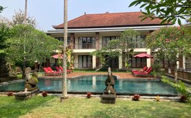 Ein ruhiger Hotelgarten mit einem Pool, umgeben von üppigem Grün und roten Liegen unter Sonnenschirmen.