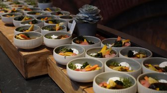 Eine lange Reihe von Schalen mit buntem Gemüse und einer cremigen Garnitur, auf einem rustikalen Holztisch angerichtet.