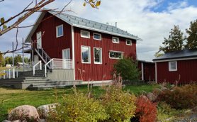 Ein rotes Holzhaus mit einem modernen Design steht in einer grünen Umgebung, umgeben von bunten Pflanzen und Steinen.