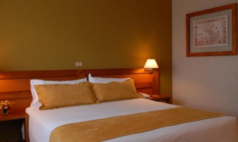 Ein gemütliches Hotelzimmer mit einem großen Bett, das mit beigen Kissen und einer Decke dekoriert ist.
