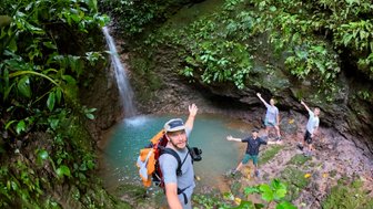 Eine Gruppe von vier Wanderern posiert fröhlich an einem kleinen Wasserfall inmitten eines üppig grünen Dschungels.