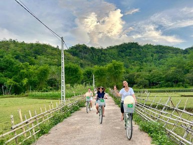 Drei Radfahrer genießen eine entspannte Fahrt auf einem schmalen Weg, umgeben von üppigem Grün und sanften Hügeln.