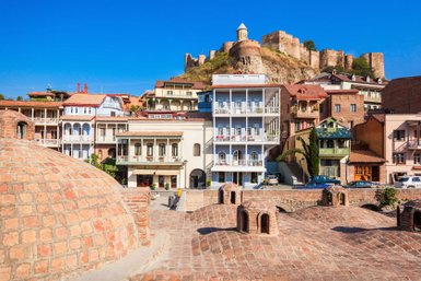 Die historische Altstadt von Tiflis zeigt bunte Häuser und die beeindruckende Festung auf dem Hügel im Hintergrund.