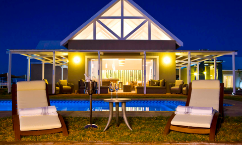 Eine Safari Lodge bei Nacht mit Pool im Vordergrund, Liegestühlen und beleuchtetem Gebäude im Hintergrund - Namibia Familienreise