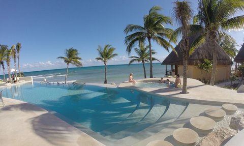 Ein einladender Poolbereich mit Palmen, wo Familienmitglieder entspannt im Wasser spielen und die Sonne genießen.