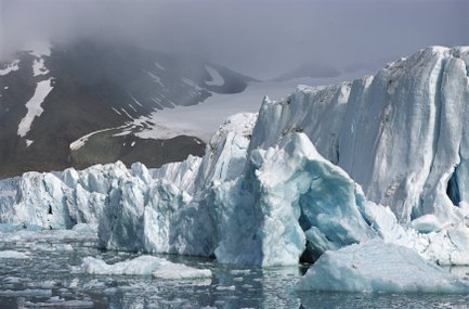Ein beeindruckender Gletscher mit blauen Eisformationen, umgeben von schneebedeckten Bergen und einem nebligen Himmel.
