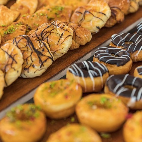 Eine Auswahl an köstlichen Gebäckstücken, darunter gefüllte Teigtaschen und schokoladene Donuts, auf einem Holzbrett.