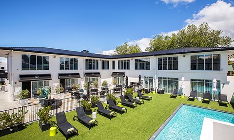 Ein modernes Boutique-Hotel mit einem einladenden Poolbereich und Liegen auf grünem Rasen unter blauem Himmel.
