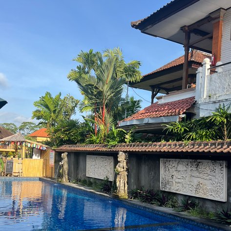 Ein glitzernder Pool spiegelt den blauen Himmel wider, umgeben von üppigem Grün und balinesischer Architektur.