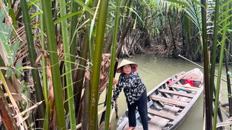 Eine Frau in einem traditionellen Hut steht auf einem Boot, umgeben von üppigem Grün im Mekong-Delta.
